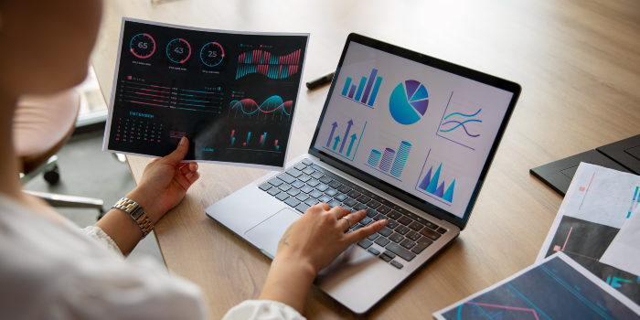 Business analyst reviewing digital dashboards and printed performance reports with data visualizations, charts, and KPIs—representing CAFM software analytics.