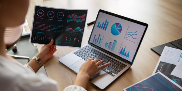 Business analyst reviewing digital dashboards and printed performance reports with data visualizations, charts, and KPIs—representing CAFM software analytics.